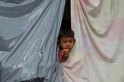 ARCHIVO - El hijo de un migrante venezolano desempleado y sin hogar se observa desde una tienda de campaña en un campamento establecido por migrantes en un parque cerca de la principal terminal de autobuses en Bogotá, Colombia, el miércoles 3 de junio de 2020. (AP Foto/Fernando Vergara)