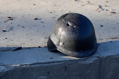 El casco de un soldado, con un agujero, cerca de los restos de camiones militares calcinados, en una calle de Kiev, Ucrania, el 26 de febrero de 2022. (AP Foto/Efrem Lukatsky)