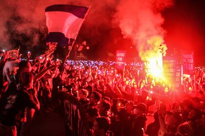 Fanáticos del fútbol encienden bengalas mientras corean lemas en Sleman, Indonesia, el jueves 6 de octubre de 2022, durante una vigilia por las más de 100 personas que murieron hace días en varias estampidas en un estadio. (AP Foto/Slamet Riyadi)