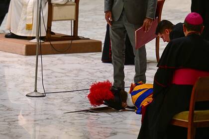 Un grupo de personas atiende a un guardia suizo que yace en el suelo tras desmayarse durante la audiencia general semanal del papa Francisco el 17 de agosto de 2022 en la sala Pablo VI del Vaticano.