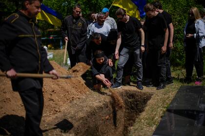 Iuliia Loseva (centro) arroja tierra sobre el féretro de su esposo, Volodymyr Losev, de 38 años, durante su entierro en el cementerio de Zorya Truda, en la región de Odesa, Ucrania, el 16 de mayo de 2022. Volodymyr Losev, un soldado voluntario ucraniano, murió el 7 de mayo cuando el vehículo militar en el que viajaba pisó una mina en el este de Ucrania. (AP Foto/Francisco Seco)