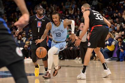 Ja Morant (12), de los Grizzlies de Memphis, maneja el balón entre los jugadores de los Clippers de Los Ángeles Reggie Jackson (1) y Robert Covington (33) en la segunda mitad del juego de la NBA, el 8 de febrero de 2022, en Memphis, Tenn. (AP Foto/Brandon Dill)