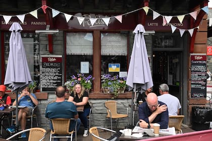 La gente se sienta frente al Relish Cafe, en el centro de la ciudad de Keswick, en el Distrito de los Lagos, al noroeste de Inglaterra, el 20 de junio de 2022, mientras un anuncio de contratación de personal aparece en la ventana del restaurante.