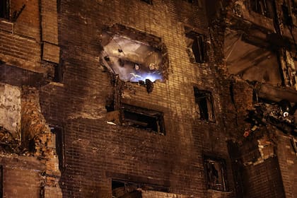 Los bomberos observan desde un edificio de apartamentos de nueve pisos parcialmente destruido después de que un avión militar Sukhoi Su-34 se estrellara en el patio de una zona residencial en la ciudad de Yeysk, en el suroeste de Rusia, el 17 de octubre de 2022