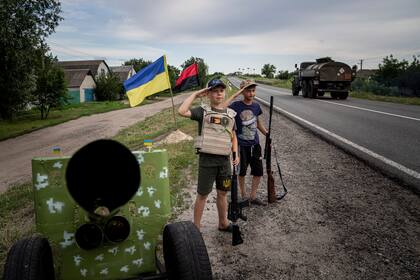 Maksym y Andrii, ambos de 11 años y con armas de juguete, saludan el paso de un convoy de soldados ucranianos en la región de Kharkiv