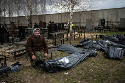 Nadiya Trubchaninova, de 70 años, sentada junto a una bolsa que contiene los restos mortales de su hijo, Vadym Trubchaninov, de 48, quien fue asesinado por soldados rusos en Bucha el 30 de marzo, a las afueras de Kiev, Ucrania, el 12 de abril de 2022. (AP Foto/Rodrigo Abd)