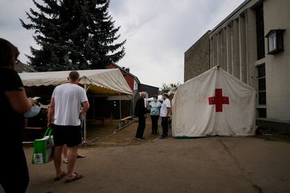 Personas hacen fila para recibir asistencia de la Cruz Roja tras las inundaciones por las intensas lluvias en Vaux-sous-Chevremont, Bélgica, el sábado 24 de julio de 2021. (AP Foto/Virginia Mayo)