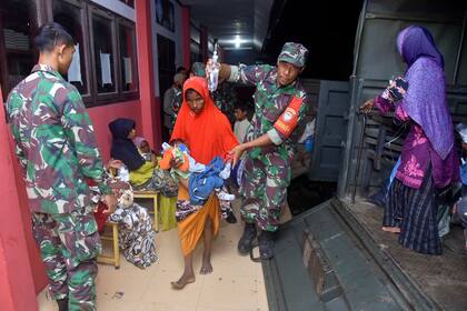 Soldados indonesios ayudan a mujeres y niños rohinyas a salir de un vehículo militar al llegar a un albergue temporal después de que su bote llegó a una playa de la provincia de Aceh, Indonesia, el lunes 26 de diciembre de 2022. (AP Foto/Rahmat Mirza)