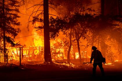 Un bombero combate las llamas que destruyen una casa en Plumas County (California), el 24 de julio del 2021. Decenas de millones de personas están siendo desplazadas de sus casas por desastres naturales asociados con el cambio climático. (AP Photo/Noah Berge, File)