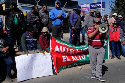 Un camionero grita consignas por un megáfono mientras otro sostiene un cartel que dice "Necesitamos dólares" mientras bloquean la carretera de El Alto a Oruro para protestar por la escasez de dólares estadounidenses y combustible en El Alto, Bolivia. (AP Foto/Juan Karita)