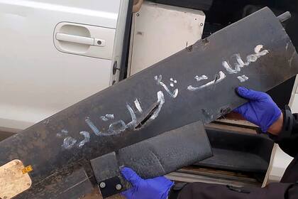 Un funcionario de seguridad sostiene parte de los restos de un dron que lleva escrito en árabe "operaciones de venganza para nuestros líderes", el lunes 3 de enero de 2022, en el aeropuerto de Bagdad, Irak. (Coalición Internacional vía AP)