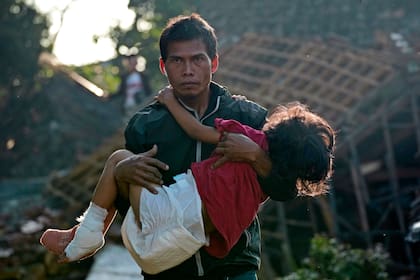 UN hombre carga a su hija herida el jueves 24 de noviembre de 2022 mientras se dirigen hacia un albergue temporal para los desplazados por el temblor del lunes en Cianjur, Java Occidental, en Indonesia. (AP Foto/Tatan Syuflana)