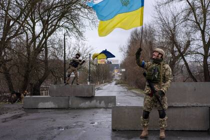 Un soldado ucraniano levanta una bandera de su país en Bucha, en las afueras de Kiev (AP Photo/Rodrigo Abd, File)