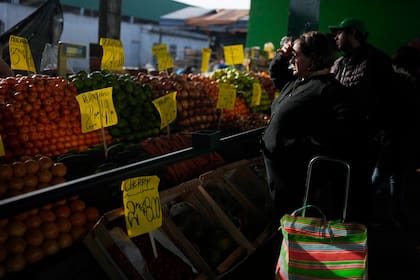 Una compradora cubre sus ojos ante los rayos de sol para revisar los precios expuestos de las frutas, en Buenos Aires