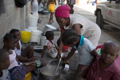 Una mujer acompañada de niños cocina en el refugio para familias desplazadas por la violencia de las pandillas en Puerto Príncipe, Haití, el jueves 9 de diciembre de 2021 (AP Foto/Odelyn Joseph)
